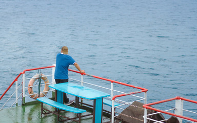 Asian man stands on baluster of ferry for relaxing and look at the ocean and island.