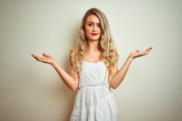 Young beautiful woman wearing casual dress standing over white isolated background clueless and confused expression with arms and hands raised. Doubt concept.