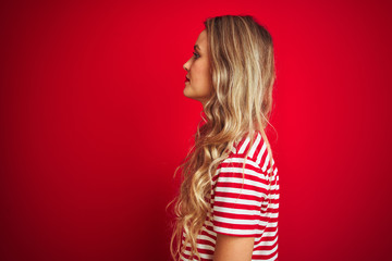 Young beautiful woman wearing stripes t-shirt standing over red isolated background looking to side, relax profile pose with natural face with confident smile.