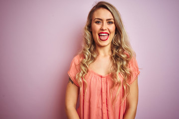 Obraz premium Young beautiful woman wearing t-shirt standing over pink isolated background sticking tongue out happy with funny expression. Emotion concept.