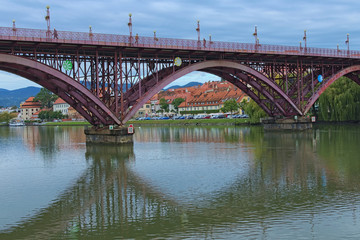 Old Bridge reflected in Drava River. Iconic landmark of city Maribor. Beautiful ancient buildings with red tile roofs at the background. Concept of landscape and nature. Maribor, Slovenia