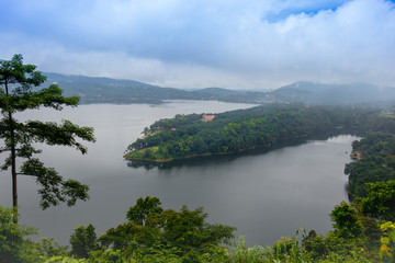 Lush green peninsula covered with thick, dense, evergreen rainforest situated in the mid of a mountain lake in overcast cloudy weather. Umaim or Bara Pani Lake, Shillong, Northeast, Meghalaya, India