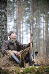 A soldier of World War II is sitting near the tree and looking up