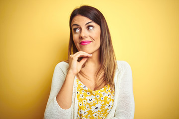 Young beautiful woman wearing jacket standing over yellow isolated background with hand on chin thinking about question, pensive expression. Smiling with thoughtful face. Doubt concept.