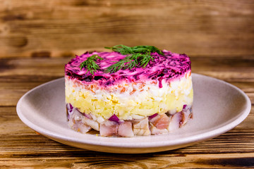 Ceramic plate with russian traditional new year salad herring under fur coat (shuba) and on rustic wooden table