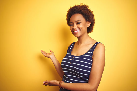 Beauitul african american woman wearing summer t-shirt over isolated yellow background Inviting to enter smiling natural with open hand