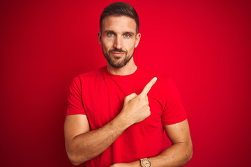 Fototapeta premium Young handsome man wearing casual t-shirt over red isolated background Pointing with hand finger to the side showing advertisement, serious and calm face