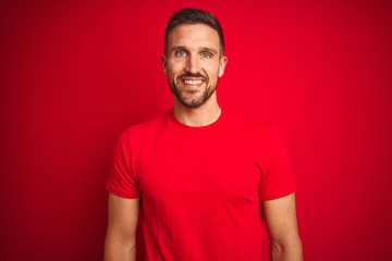 Young handsome man wearing casual t-shirt over red isolated background with a happy and cool smile...