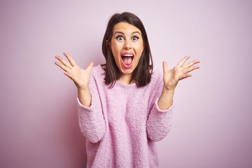 Young beautiful brunette woman wearing a sweater over pink isolated background celebrating crazy and amazed for success with arms raised and open eyes screaming excited. Winner concept