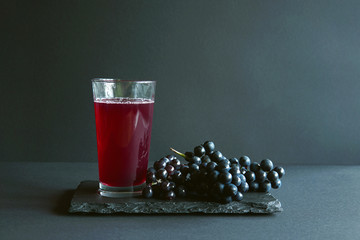 A glass of fresh grape juice and isabella grape on a stone plate, dark background, free space for...