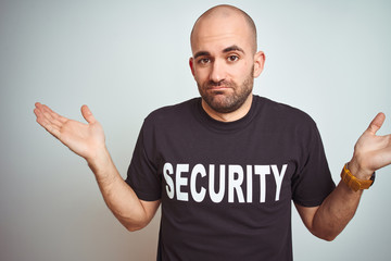 Naklejka premium Young safeguard man wearing security uniform over isolated background clueless and confused expression with arms and hands raised. Doubt concept.