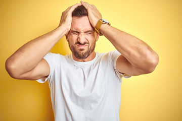 Fototapeta na wymiar Young handsome man wearing casual white t-shirt over yellow isolated background suffering from headache desperate and stressed because pain and migraine. Hands on head.