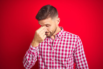 Young handsome man over red isolated background tired rubbing nose and eyes feeling fatigue and headache. Stress and frustration concept.