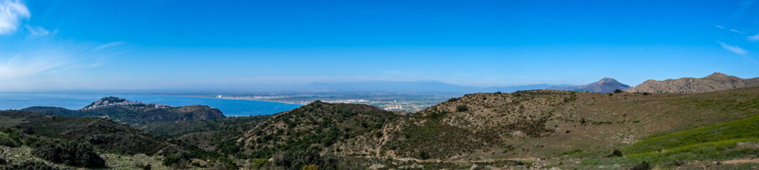 Fototapeta na wymiar Mountain landscape in Roses, Catalunya, Spain. Mountain covered with green grass and shrubs on blue sky and sea background. Panoramic view, natural background. The bay and the city in the background.