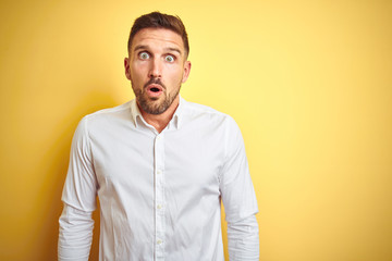 Young handsome man wearing elegant white shirt over yellow isolated background afraid and shocked with surprise expression, fear and excited face.