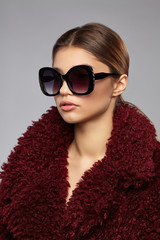 Close-up shot of brunette European lady in burgundy-coloured furs and butterfly sunglasses with...