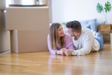 Young beautiful couple in love moving to new home, lying on the floor around cardboard boxes, very happy and cheerful for new apartment