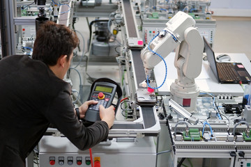 Man is holding teach panel to control a robotic arm which is integrated on smart factory production...