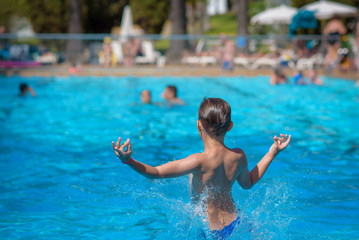 European boy  jumping into swimming pool at resort. Moment of entrance in water. He has fun during his summer holidays.