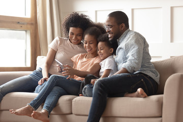 Happy black family with kids relax on sofa with tablet