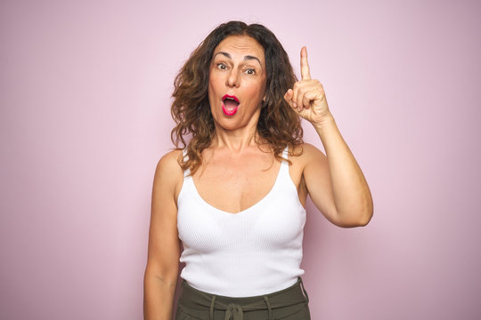 Middle age senior woman standing over pink isolated background pointing finger up with successful idea. Exited and happy. Number one.