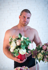 Sexy male athlete with bouquets of flowers on white background.