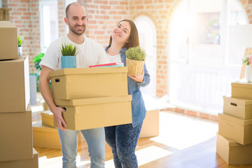 Young couple moving to a new home, smiling happy holding cardboard boxes