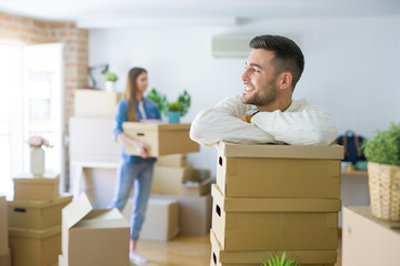 Young couple moving to a new home, handsome man smiling leaning on cardboard boxes