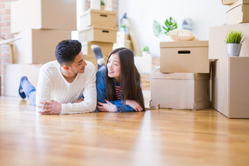 Young asian couple lying on the floor of new house arround cardboard boxes relaxing and smiling...