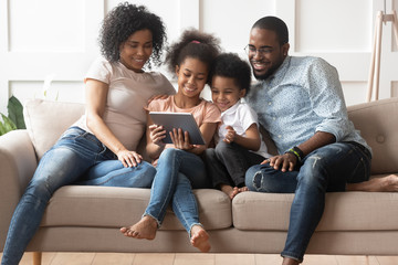 Happy parents with kids relax on sofa with tablet