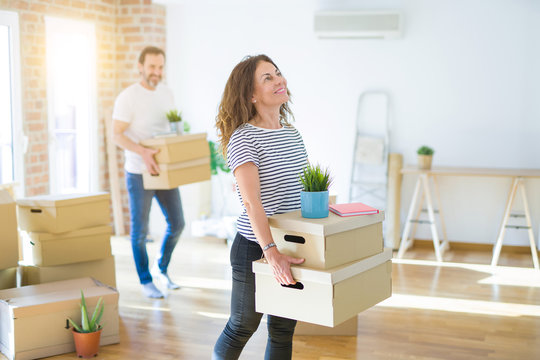 Middle age senior couple moving to a new house, smiling woman holding cardboard boxes and packaging