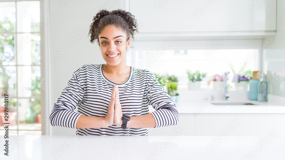 Sticker Beautiful african american woman with afro hair wearing casual striped sweater praying with hands together asking for forgiveness smiling confident.