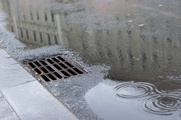 Autumn asphalt, metal grating stormwater on a city street. Autumn rainy weather with puddles, outflow of water from the highway. backdrop texture background