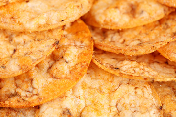 Extreme close up of a pile of organic, crispy, baked, whole grain rice chips with tomato and paprika spices. Gluten free healthy snack. Macro food background.