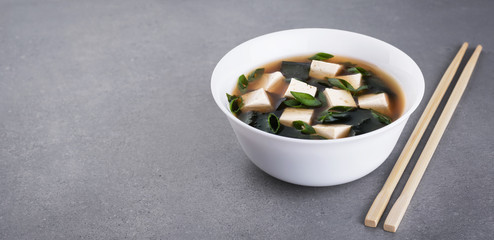 Bowl with miso soup and chopsticks on a gray background.