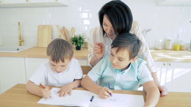 Young mother helping her sons to draw with colored markers. Preschool education