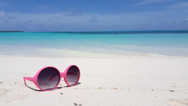 Still video of pink sunglasses lying on white beach on blur oceanic background in Australia