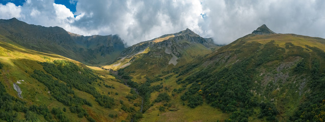 Panorama of mountain terrain in early autumn; amazing dramatic clouds on mountain peaks; rivers cutting gorges and canyones in valleys; natural outdoor travel background; sunny day on Caucasus