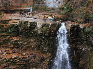 man with woman holding ukrainian flag on the top of the waterfall