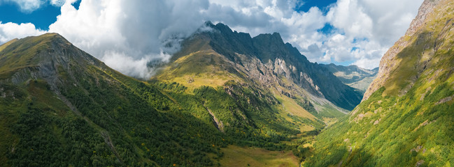 Panorama of mountain terrain in early autumn; amazing dramatic clouds on mountain peaks; rivers cutting gorges and canyones in valleys; natural outdoor travel background; sunny day on Caucasus