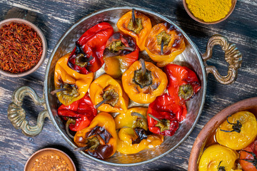 Baked red and yellow tomato and bell pepper. Tomatoes and bell peppers in a baking dish on a wooden table. A healthy and delicious vegetarian dish. Closeup, top view