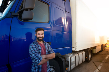 Professional truck driver with crossed arms standing by his semi truck. Trucker occupation and...