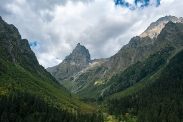 Fototapeta na wymiar Panoramic view of river Malaya Laba valley with mountain ranges on sides, sharp peak Igolchatiy; morning landscape, dramatic cloudy sky, deep pine fir forest; danger narrow gully, steep gradient