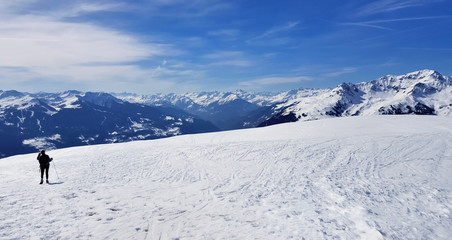 Fototapeta na wymiar little silhouette of a hiker in snowy mountain under blue sky