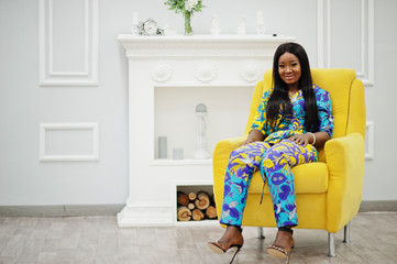 Elegance african american woman model wear in colored clothes. Chic afro women in room sitting on yellow chair.