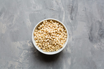 Pine nuts in white bowl on gray concrete background. Organic healthy food concept. Flat lay, top view, mockup, overhead, template, view from above