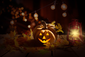 Halloween or Thanksgiving background with fresh fall pumpkins on straw lit by a burning lantern and sparkling part lights behind with copy space