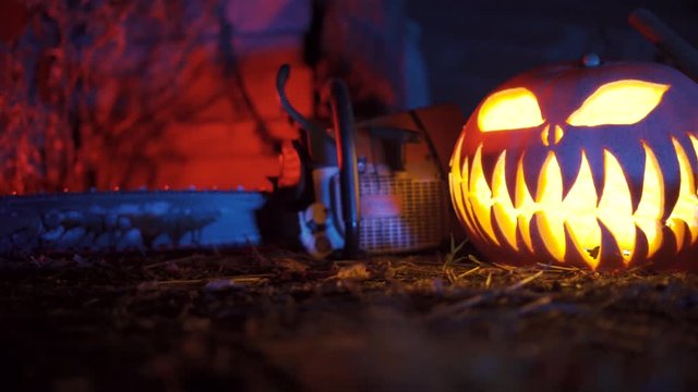 Bloody chainsaw is laying next to an axt and a glowing pumpkin.
