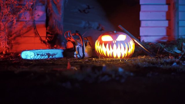 Bloody chainsaw is laying next to an axt and a glowing pumpkin.