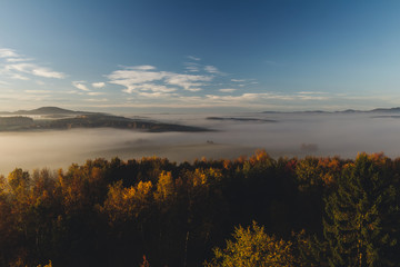 Aerial view to autumn foliage trees with misty fog and hill in sunrise, Czech landscape, toned photo